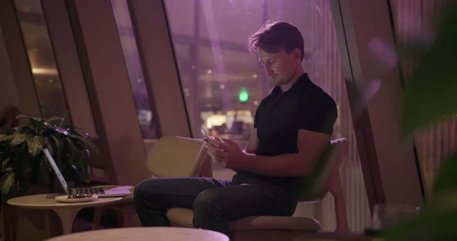 A man sits down by a window looking at his phone