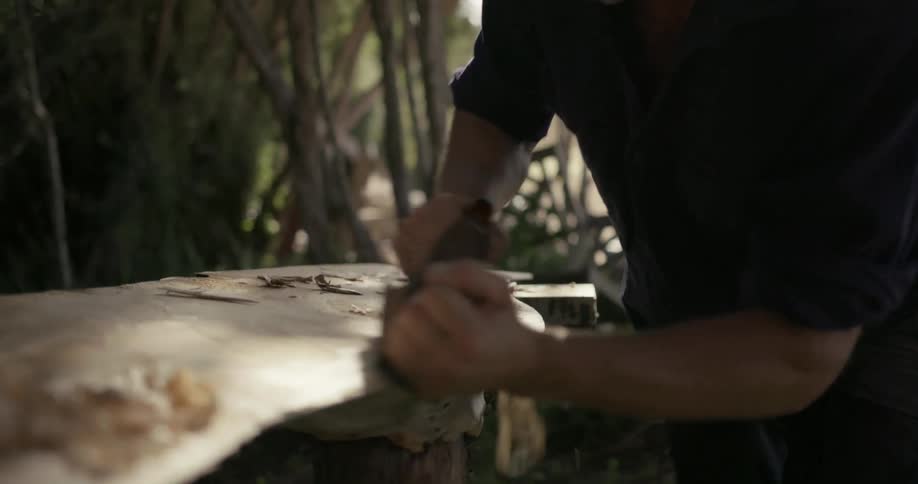 Man sanding piece of wood with sanding tool outside during the say