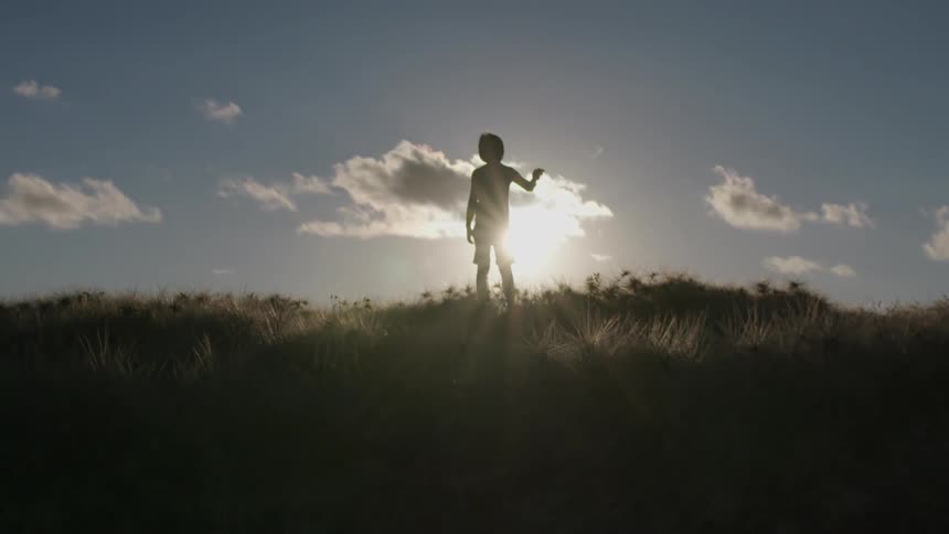 A child is standing on the hilltop at sunset