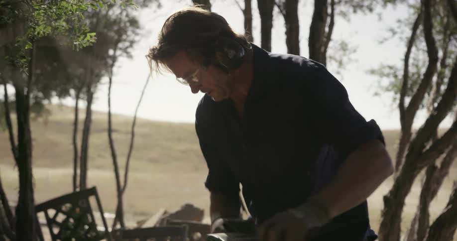 Man outside in yard using electric sander to sand piece of wood