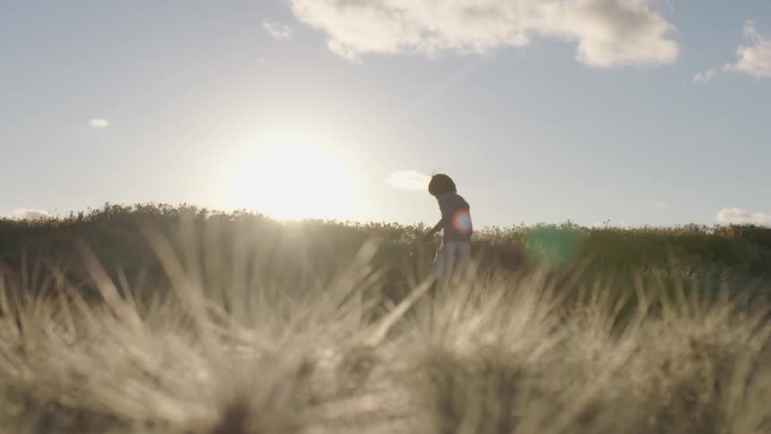 A girl walks across a field full of spiky grass