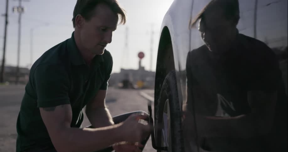 Man changes tire of his car on a sunny day