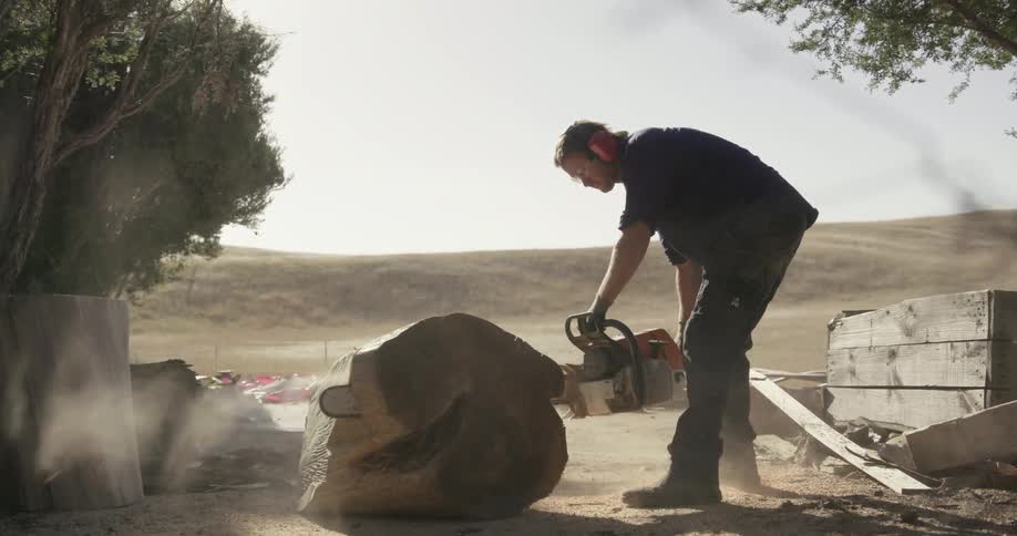 Man saws through large piece of wood outside