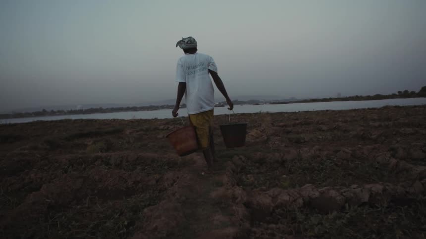 A woman hauls buckets towards a lake