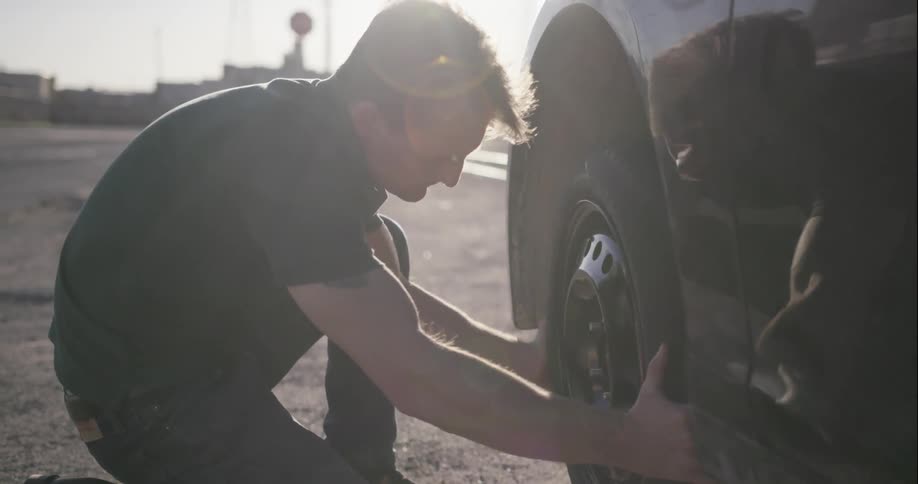 A man changes a tire on the side of the road