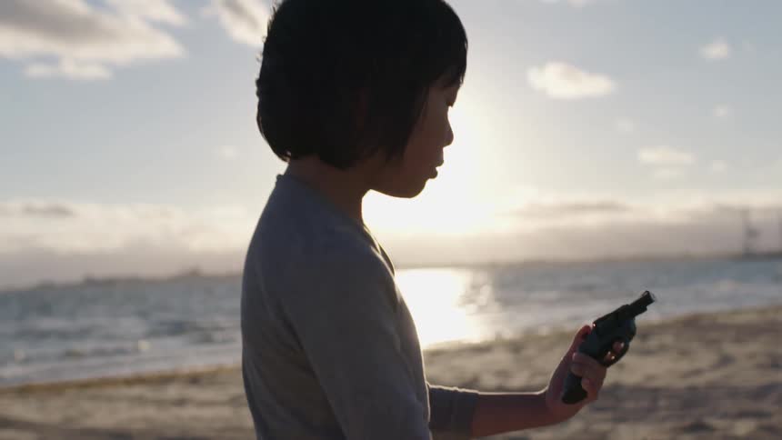 A young boy plays with a toy gun on the beach