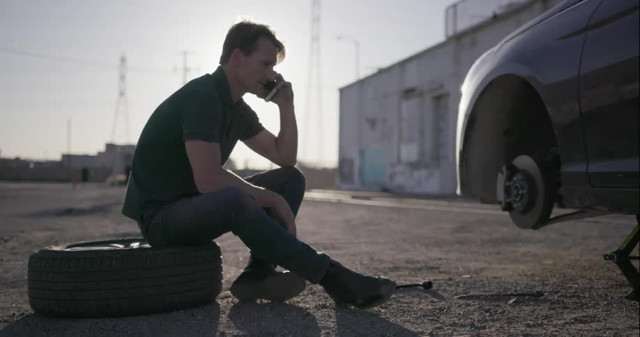 A man is sitting on a tire on the side of the road