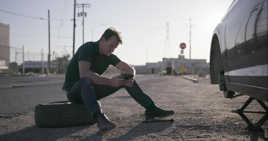 A man sits on a tire and makes a phone call
