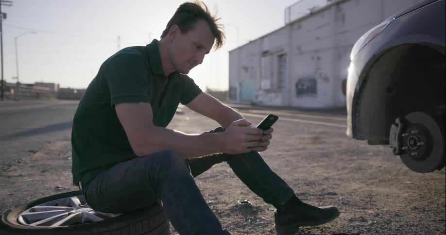 A man is sitting down on a wheel using his phone