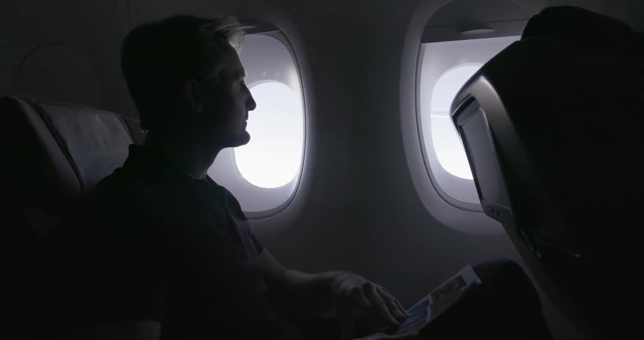 Man on an airplane reads a magazine and looks out the window