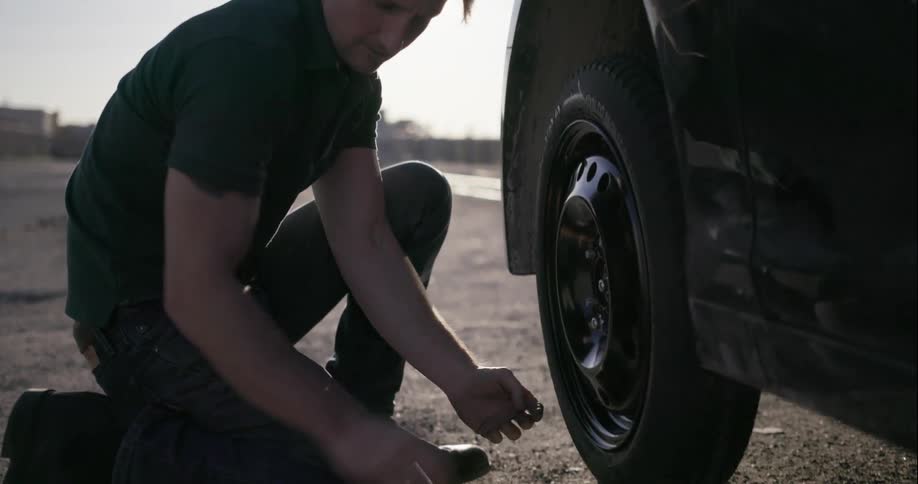 A man changes a car tire on the side of a road