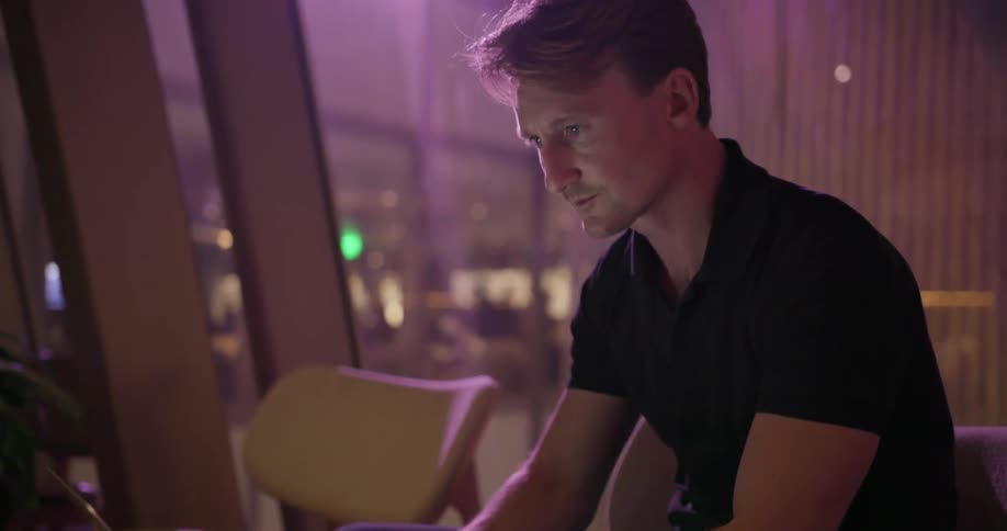 Man sits in a dark building typing on a laptop