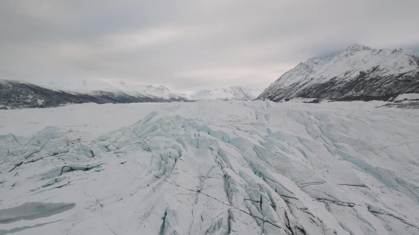Traverse along a frigid glacial ice flow between snow covered mountains