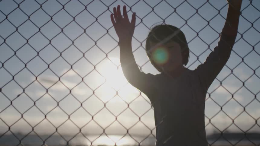 A young boy stands in front of a steel fence