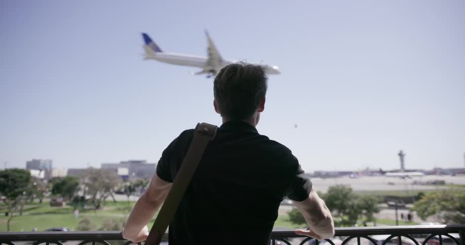 A man stands at a balcony and watches a plane land