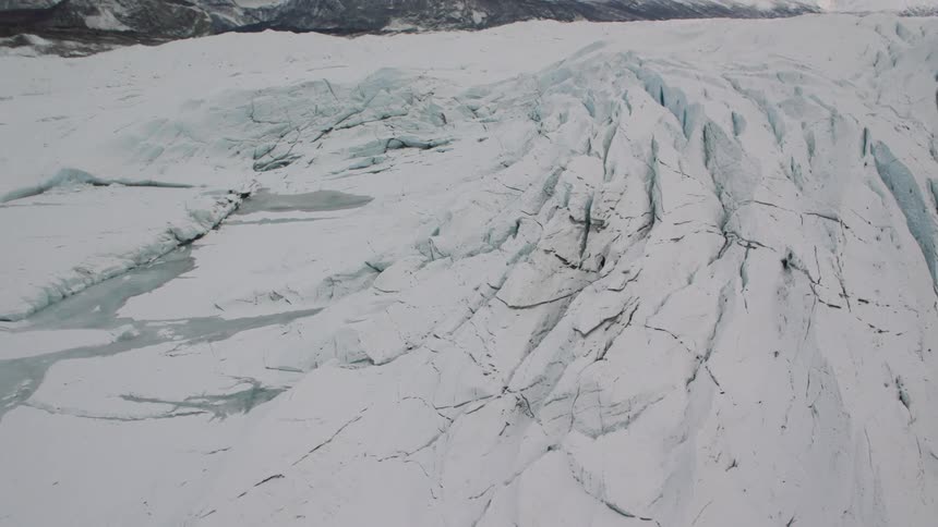 Tilt up reveal of mountains behind the cracked ice of a snow covered glacier