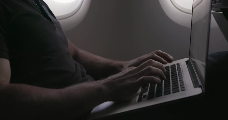 Man sitting in airplane is typing on a laptop