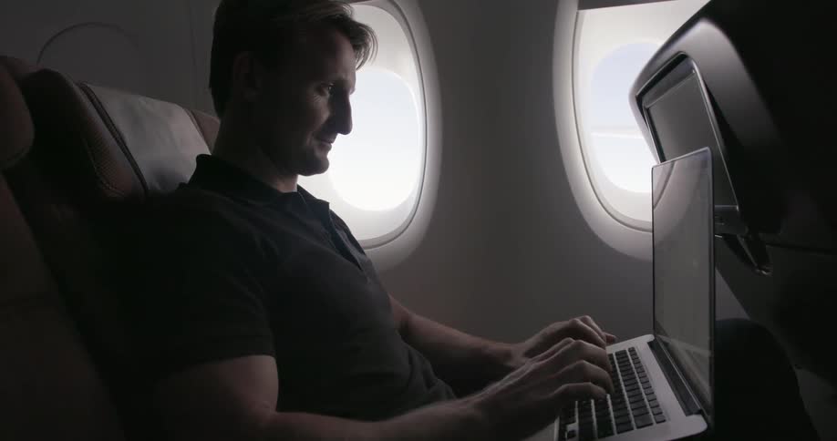 A man types on a laptop while riding in a plane