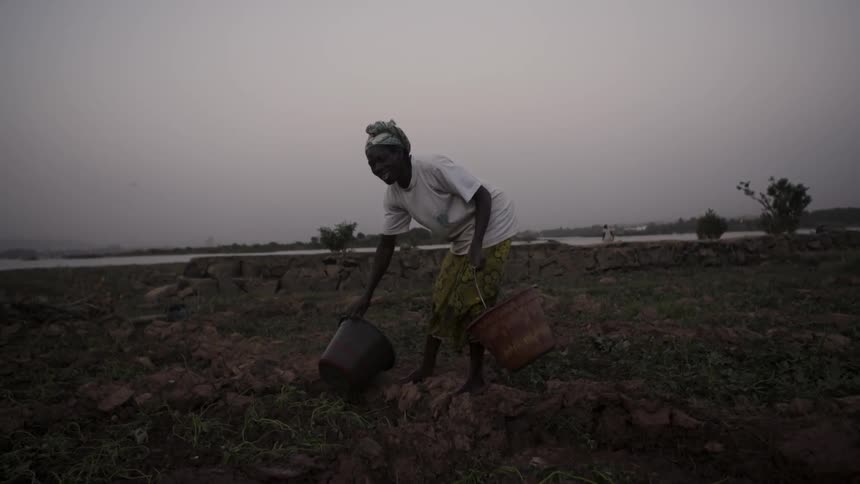 A woman picks up and carries empty water buckets
