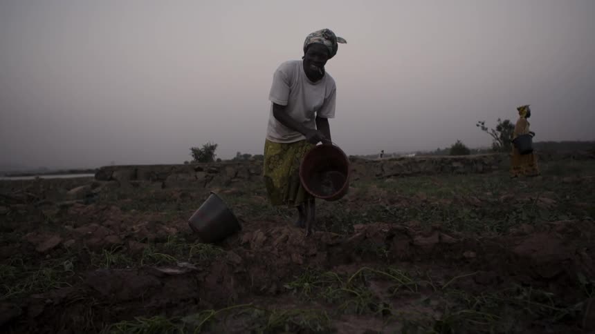 A bucket of water is dumped in a dirt field at sunset