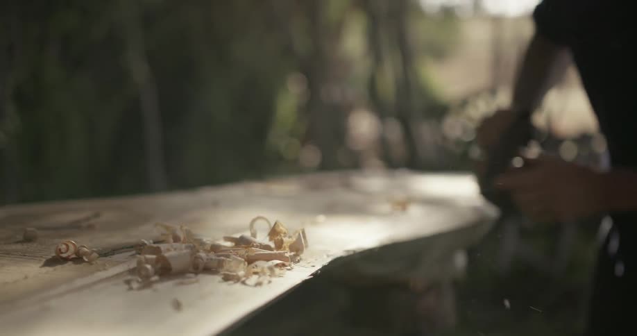 A carpenter uses a tool to shave and smooth a piece of wood