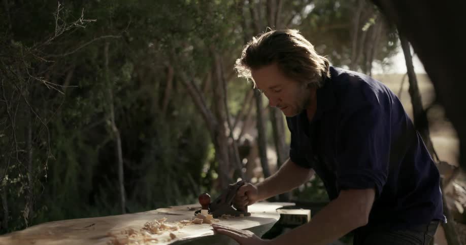 A man is using a planer as he works a piece of wood