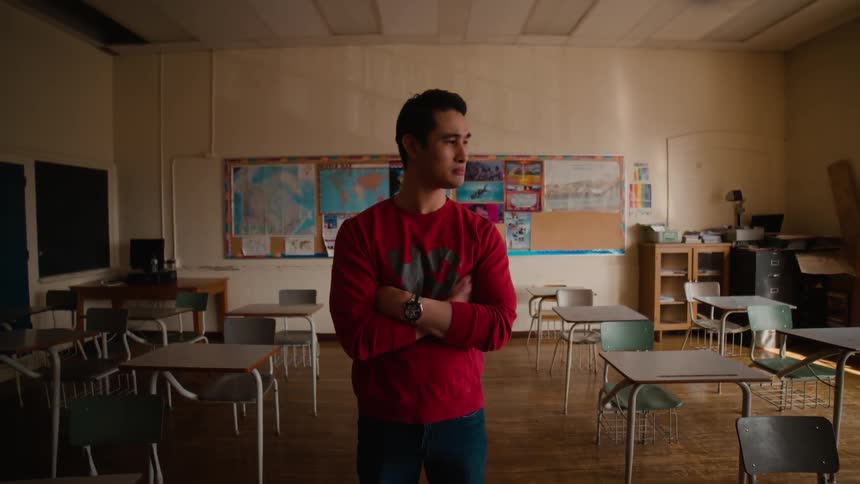 A man is standing in a classroom with his arms folded