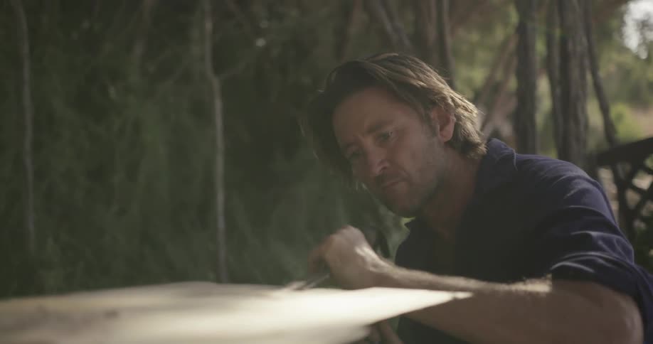 A man carves a piece of wood outdoors