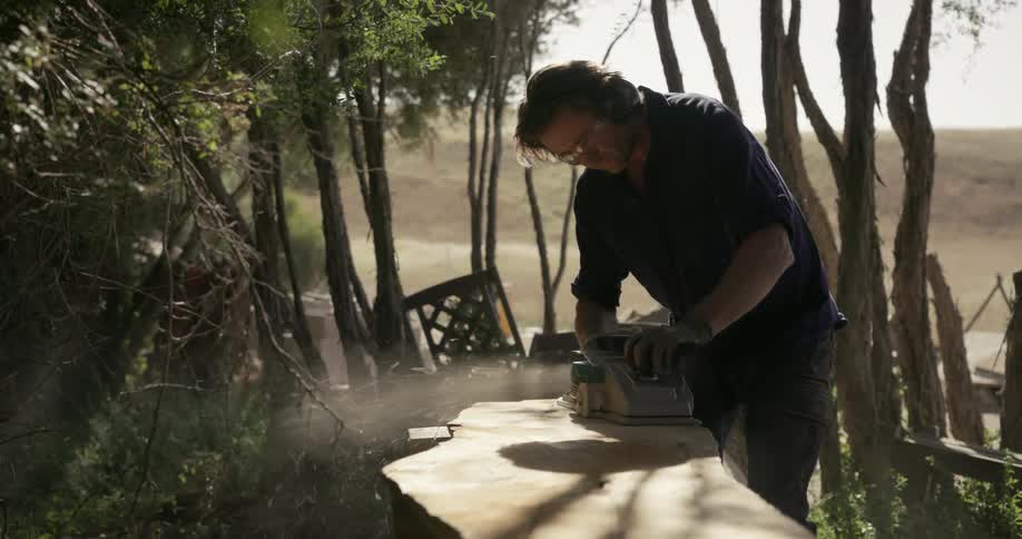 A man carves a piece of wood outdoors