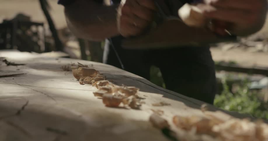 A carpenter shaves a piece of wood with a hand tool