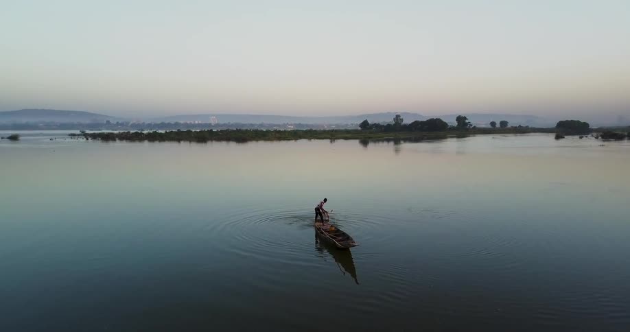 A man is paddling a small boat at dusk