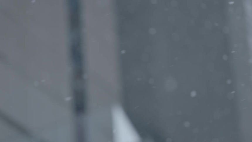 Snow falls around buildings in a city