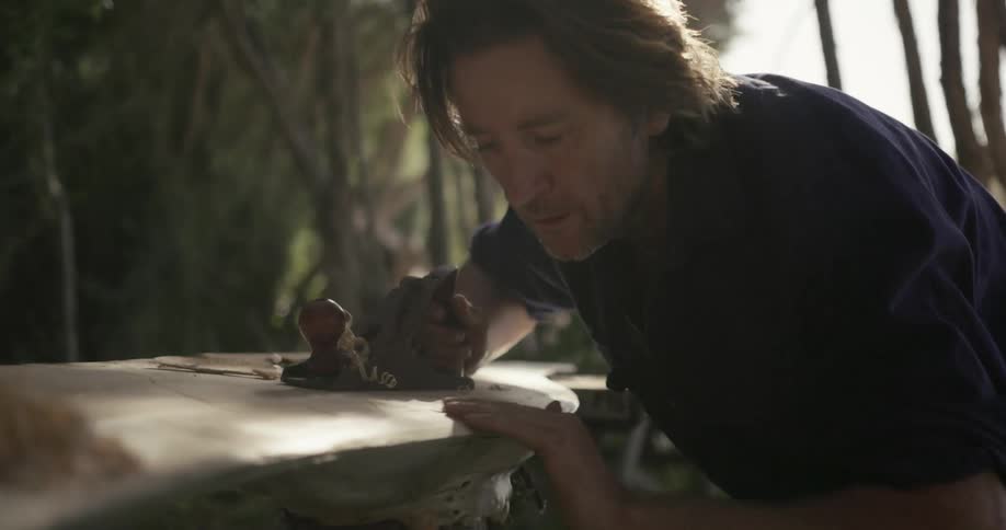 A man is using a hand planer to sculpt a piece of wood