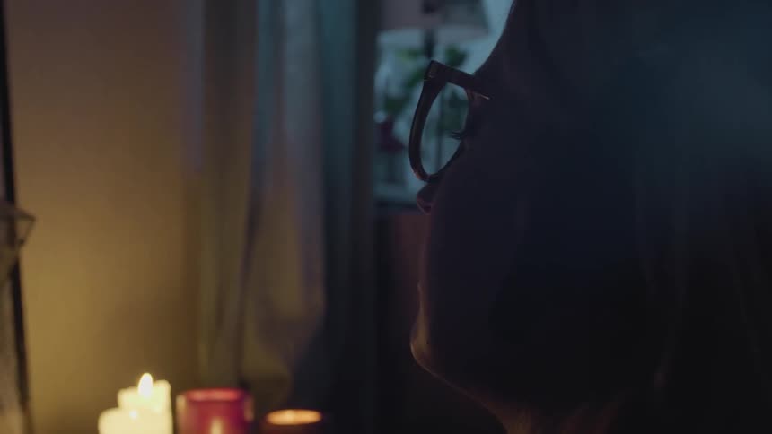 A woman sways slightly as she sits near some candles