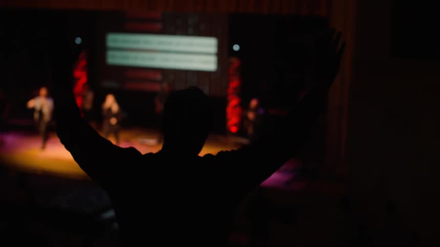 A man stands with arms raised to celebrate the singers on stage