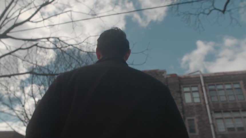 A man in a dark jacket walks toward a building