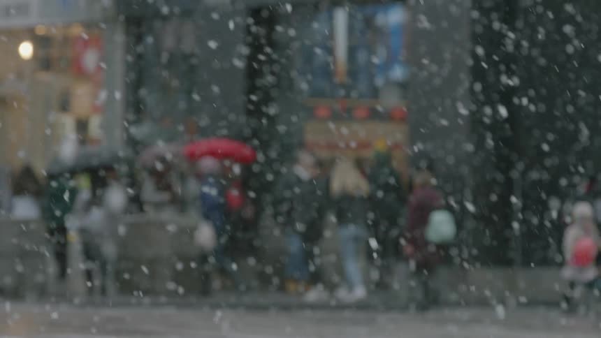 People walking in the downtown of a city while snow falls