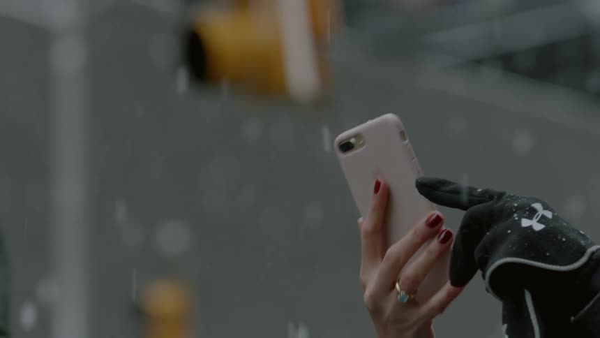 Woman outside in city taking picture with cell phone while it snows