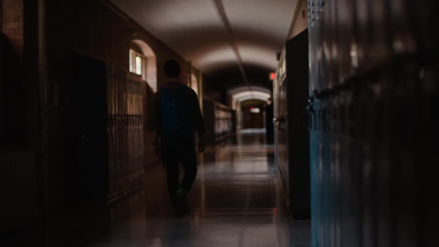 Man wearing backpack walking down school hallway lined with lockers