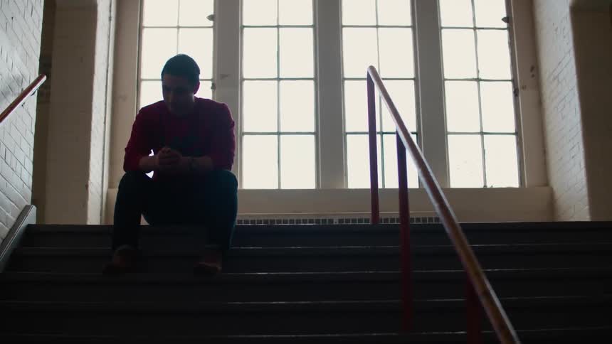 Man sits at the top of a flight of stairs indoors