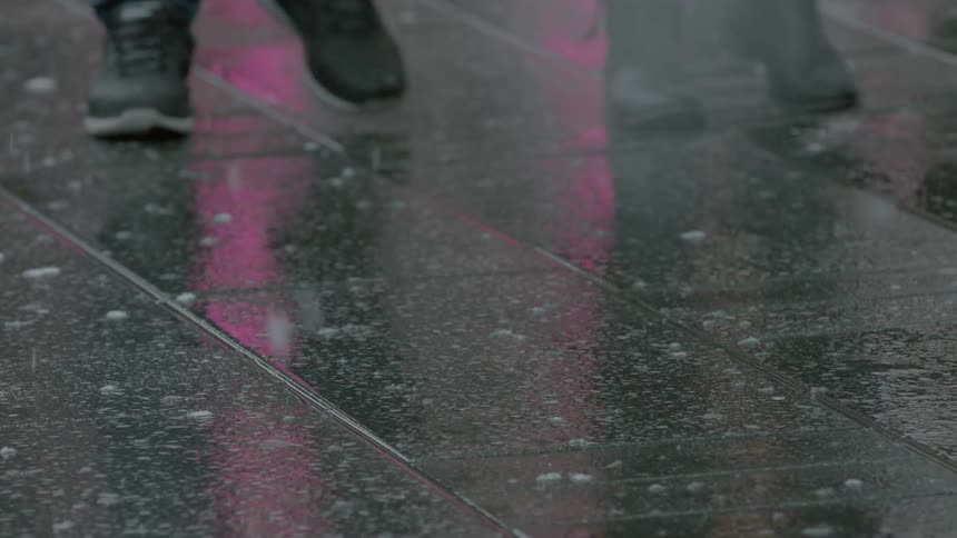 View of people's feet as they walk on the sidewalk as snow falls