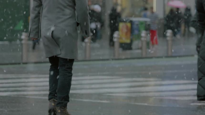 People and cars cross a city intersection on a snowy day
