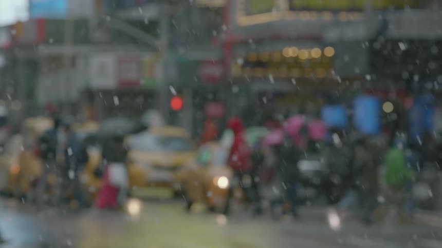 People walk across the street in the city as it snows