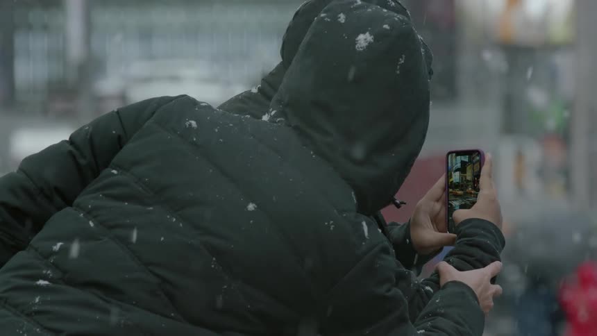 A man takes a picture in a city while it snows