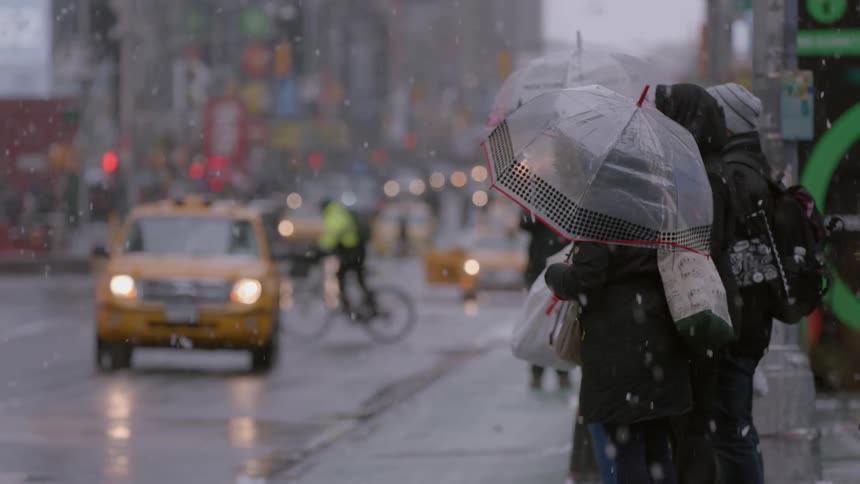 People travel down a busy city street as it snows