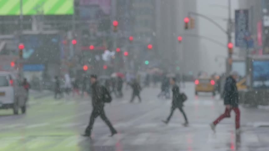 Pedestrians cross a city street while it snows