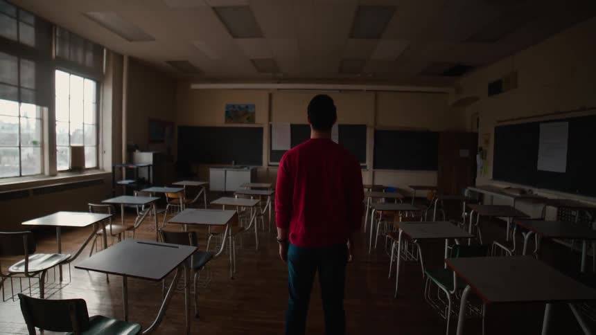 A man in red stands in an empty classroom