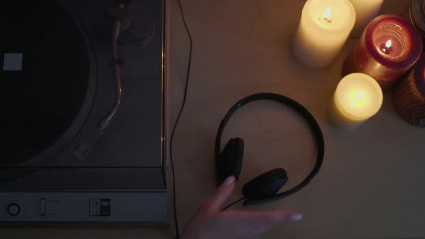 Woman picks up headphones next to record player machine and candles