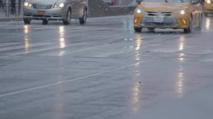 Cars drive down the street as it snows