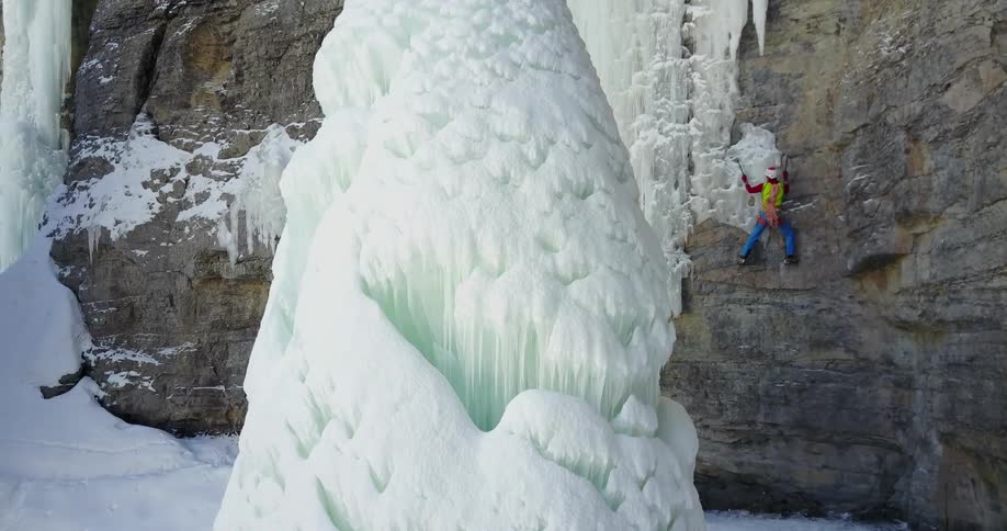A man is climbing sideways onto the ice on a cliff
